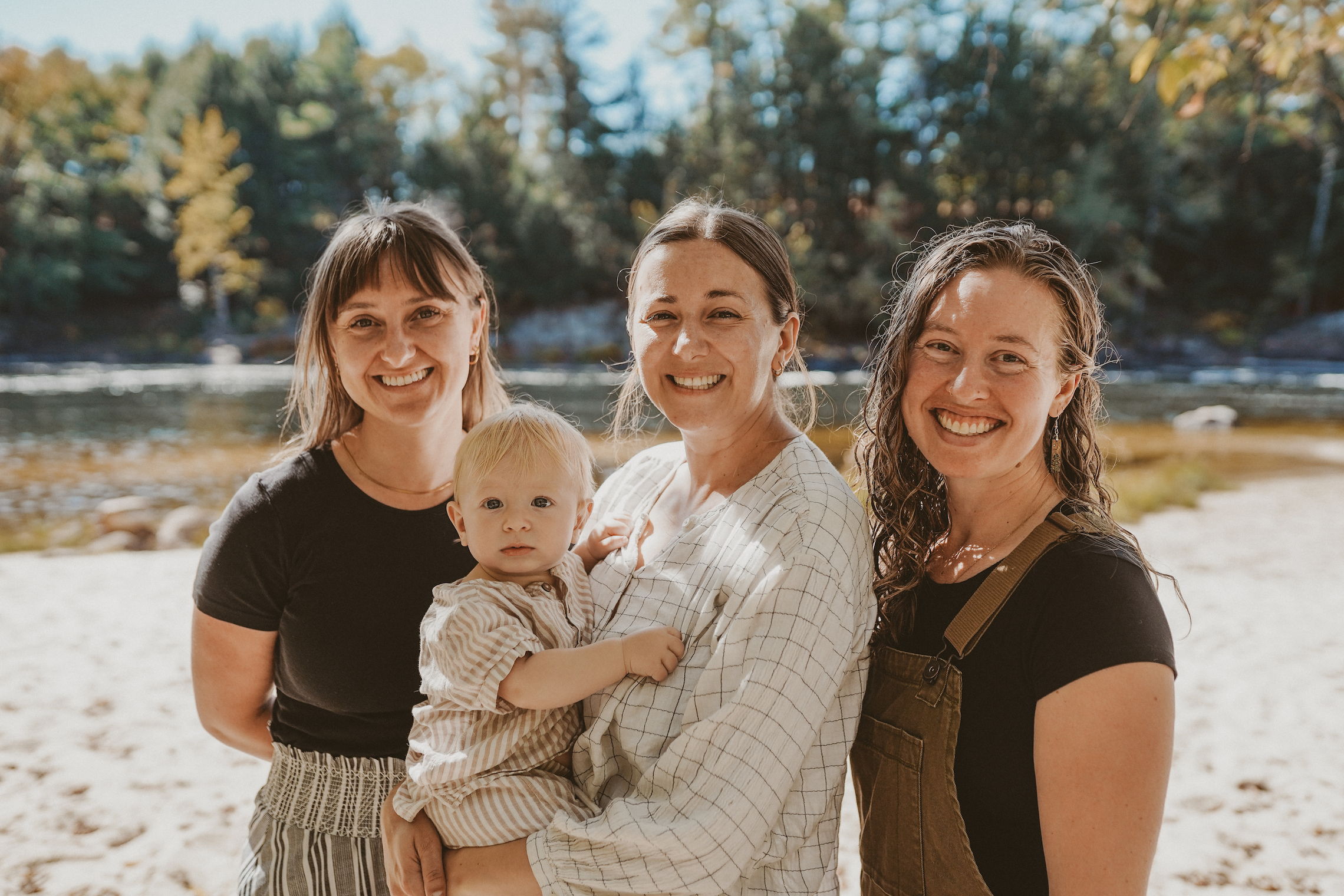 The Midiwives 3 Midwives, smiling in front of river, holding baby