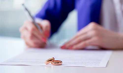 woman signing paper with wedding rings laying on the contract