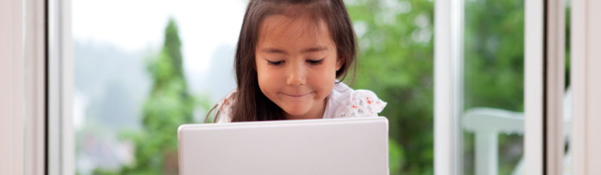 Young girl smiles at laptop.