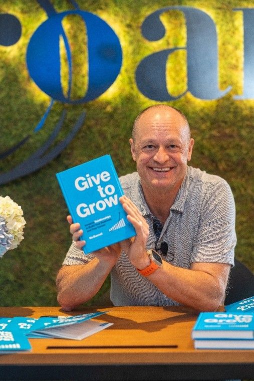 Mo Bunnell sitting at a table holding his book, Give to Grow
