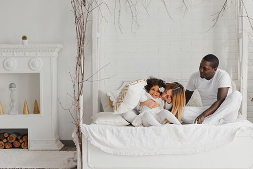 happy-interracial-couple-with-their-little-daughter-at-home-bedroom