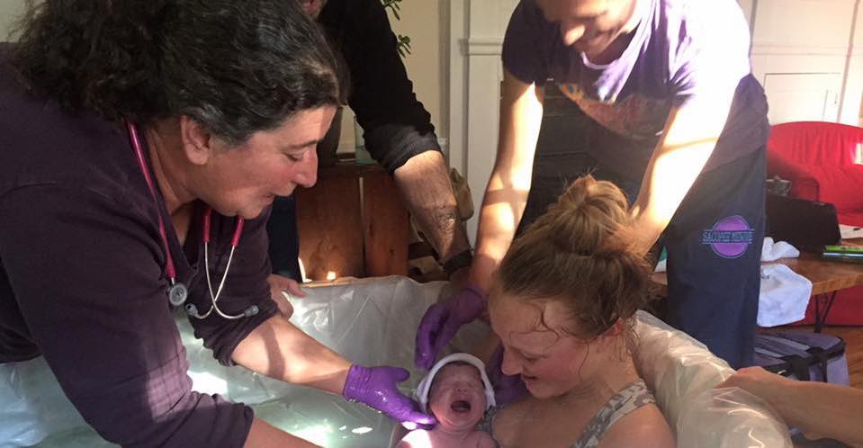 Midwife helping mom and newborn in birth tub