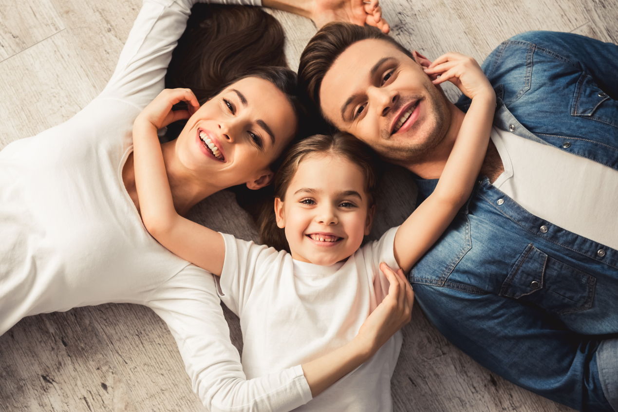 a man in a denim shirt with a white tshirt is laying in the floor with a woman and young girl both wearing white tshirts