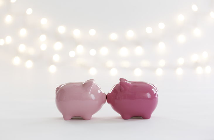 Two pink piggy banks sharing a kiss under string lights