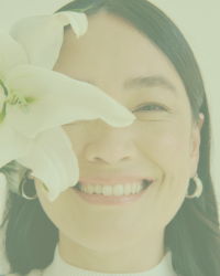 woman smiling with large white flower blocking half her face