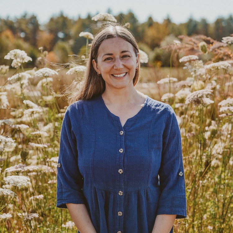 Young woman in blue button-down dress standing in front of field of flowers