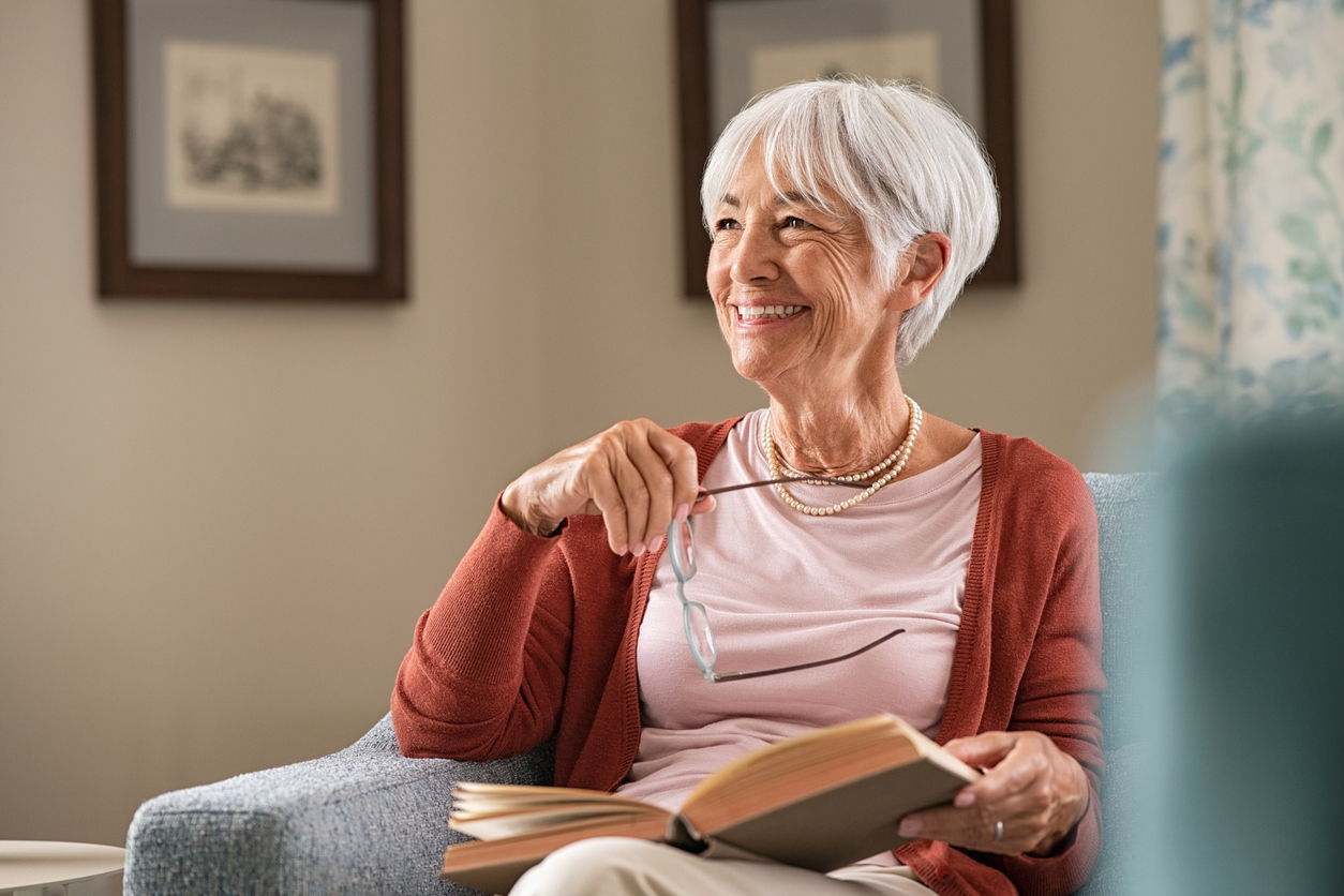 mature female sitting on couch with book and reading glasses looking off