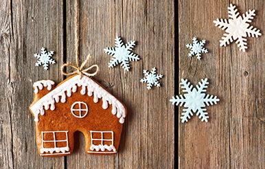Holiday Spending Gingerbread house on string with snowflakes against a wooden background