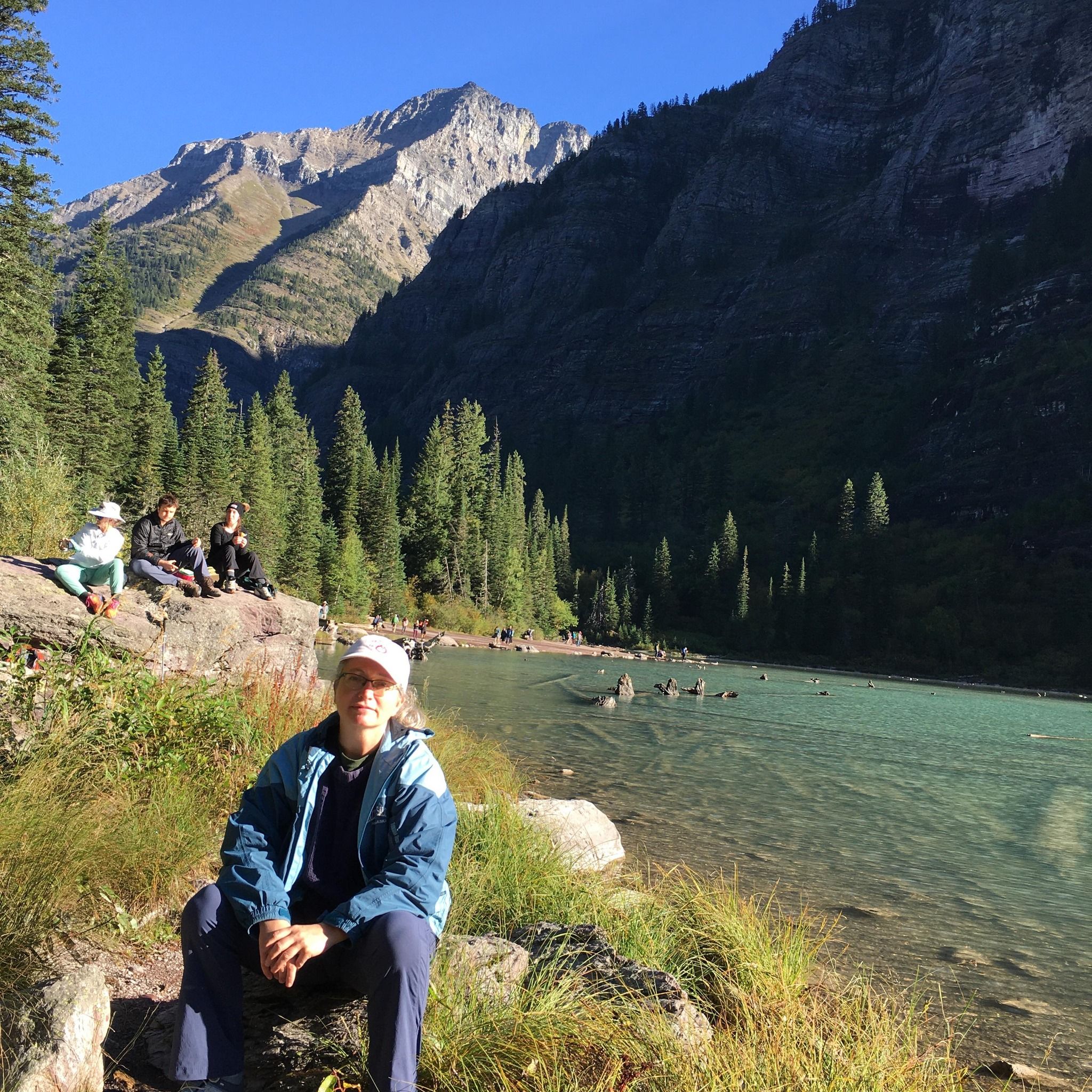 Woman sitting on rock by pond in front of mountains