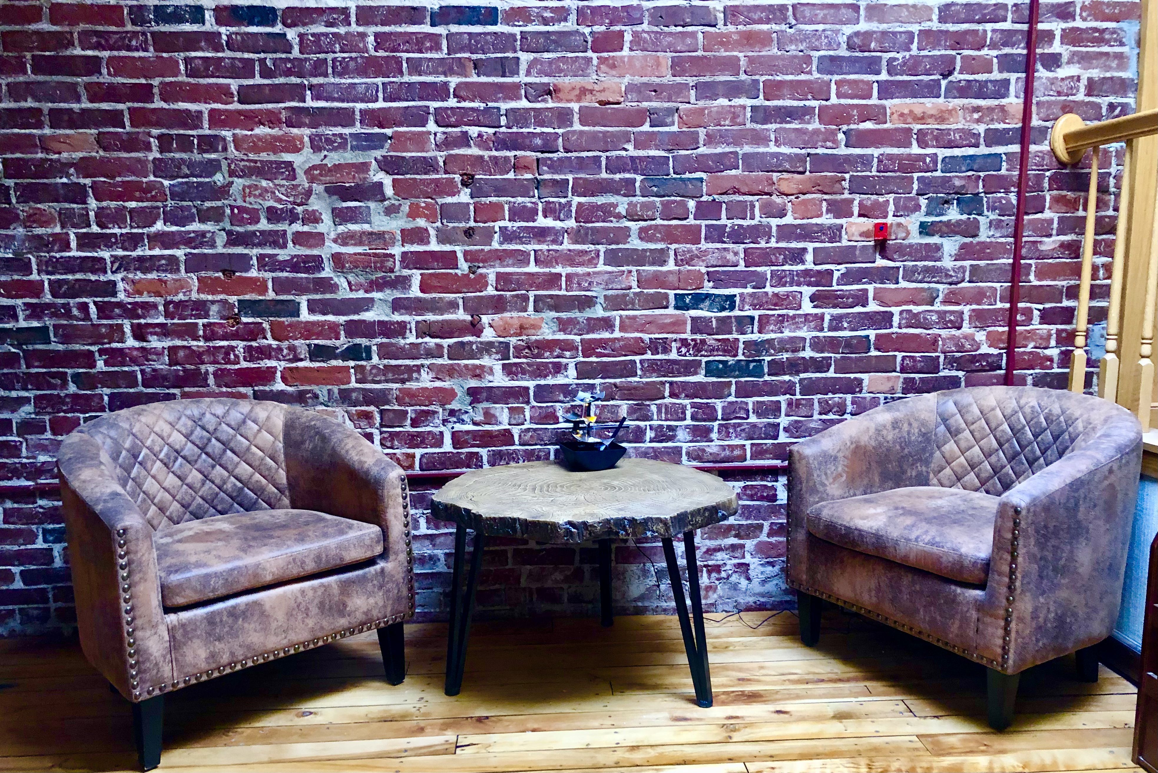 Two brown leather chairs in front of brick wall