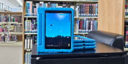 A stack of iPads in blue cases sit on a black table. One iPad is propped up and displays an app for learning the night sky.