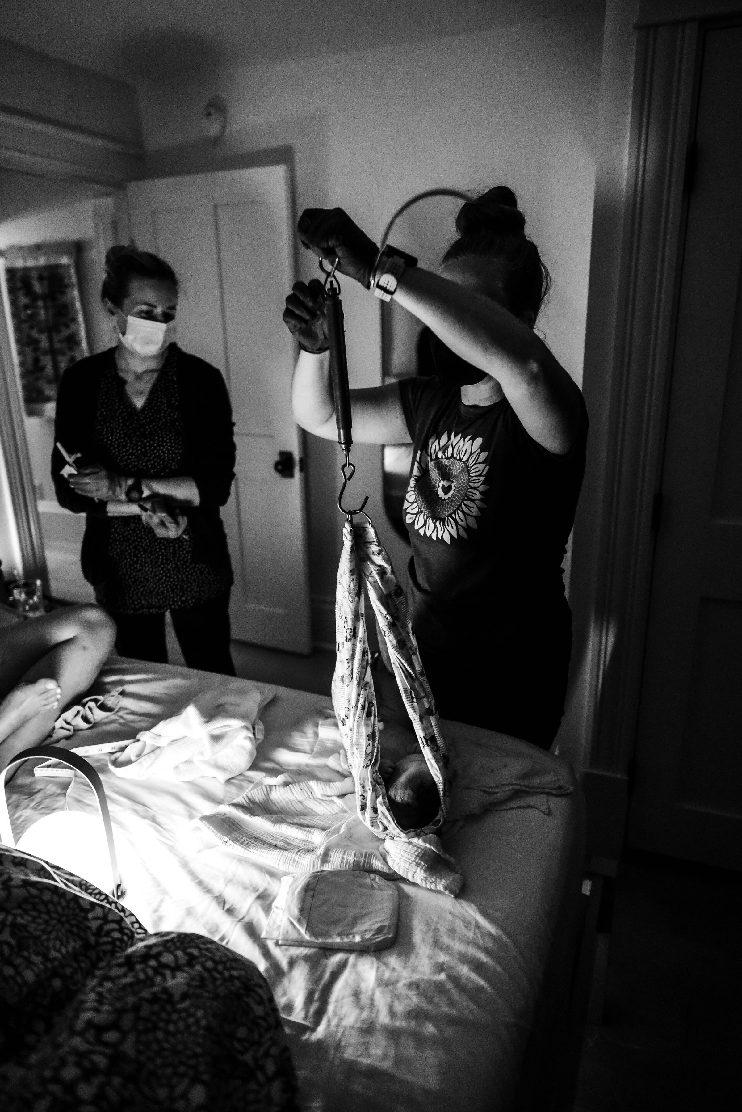 Black and white image of midwife weighing newborn baby