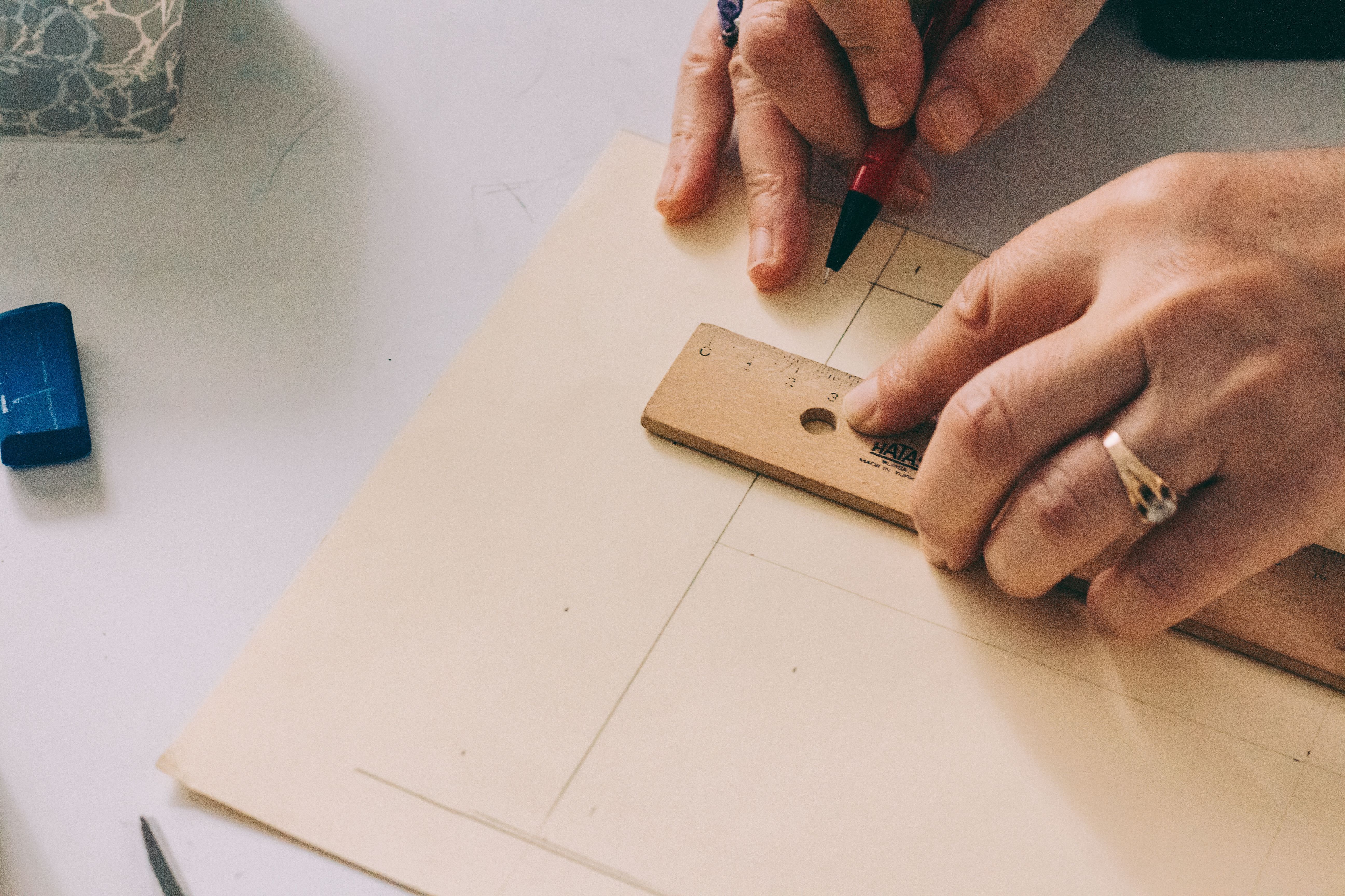 Hands drawing measured lines on paper with a wooden ruler and pencil.