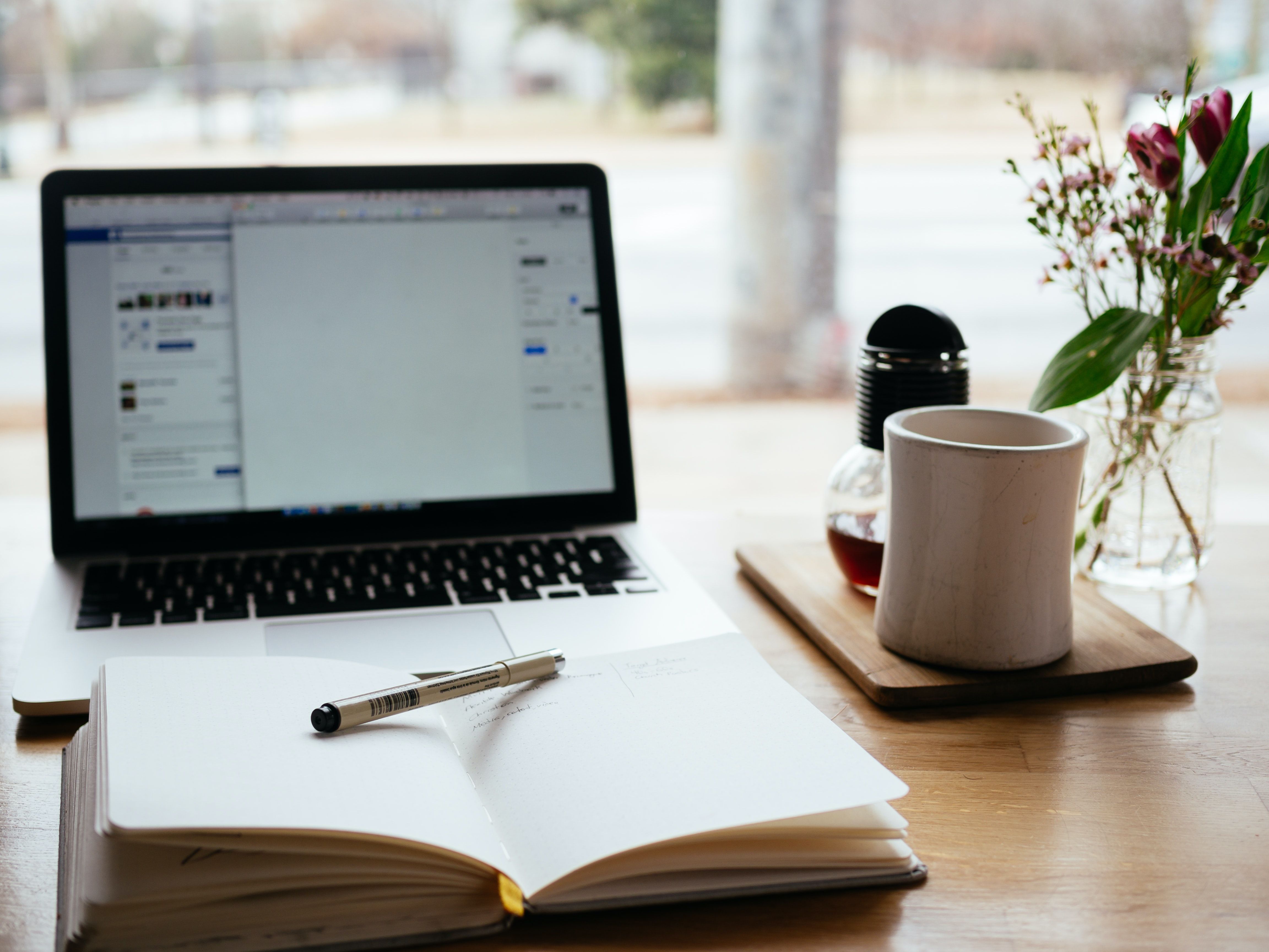 Desk with laptop, open notebook and pen, and coffee mug