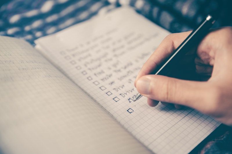 Courtesy of glenn-carstens-peters from unsplash Hand holding a pen writing a to-do list on a graph paper notebook