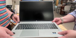 Computers and Printing Hands holding an HP laptop computer and passing it to another set of hands. A person in the background sits at a table and looks at a computer.