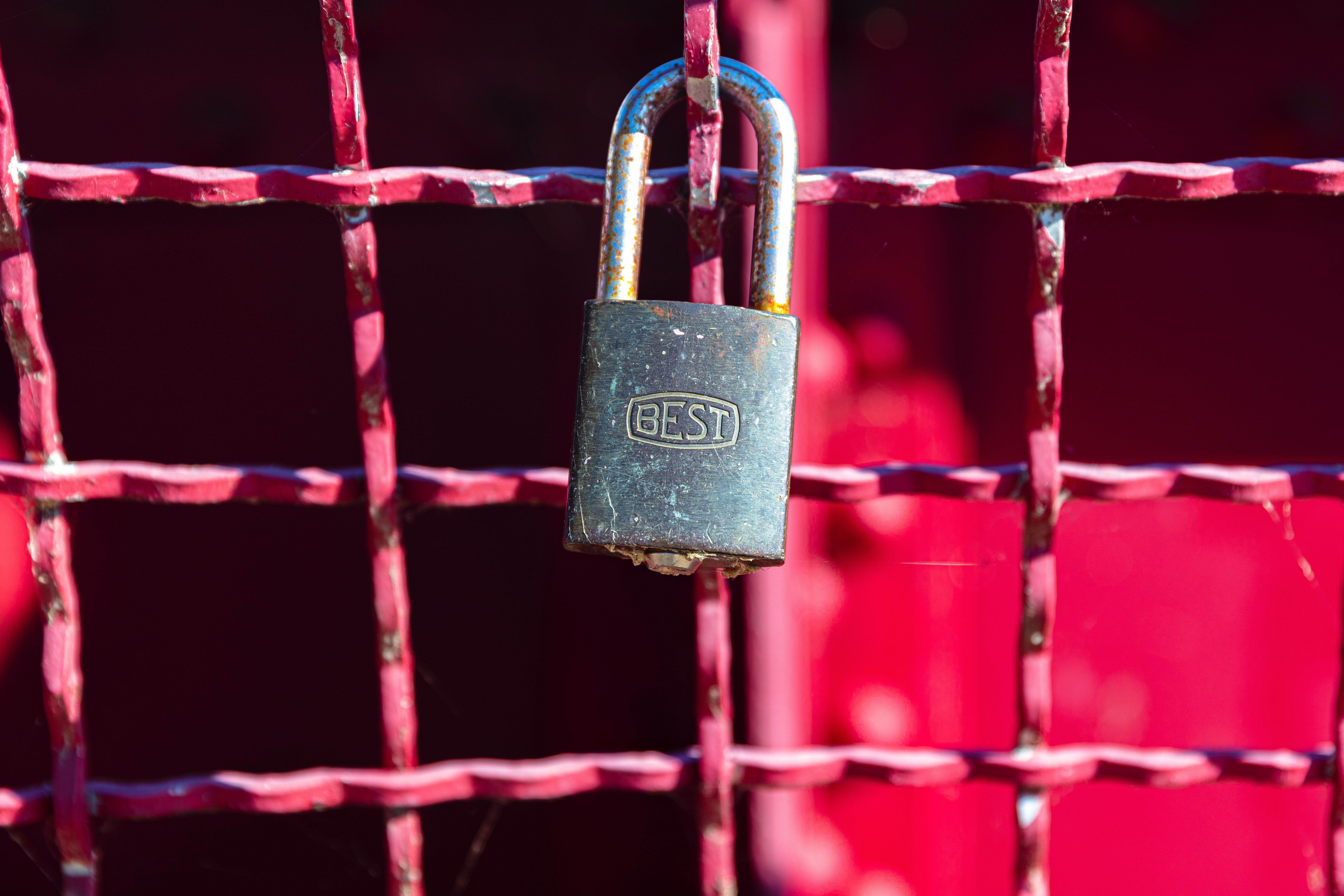 Courtesy of jon-moore from unsplash Small metal lock on a painted red metal gate