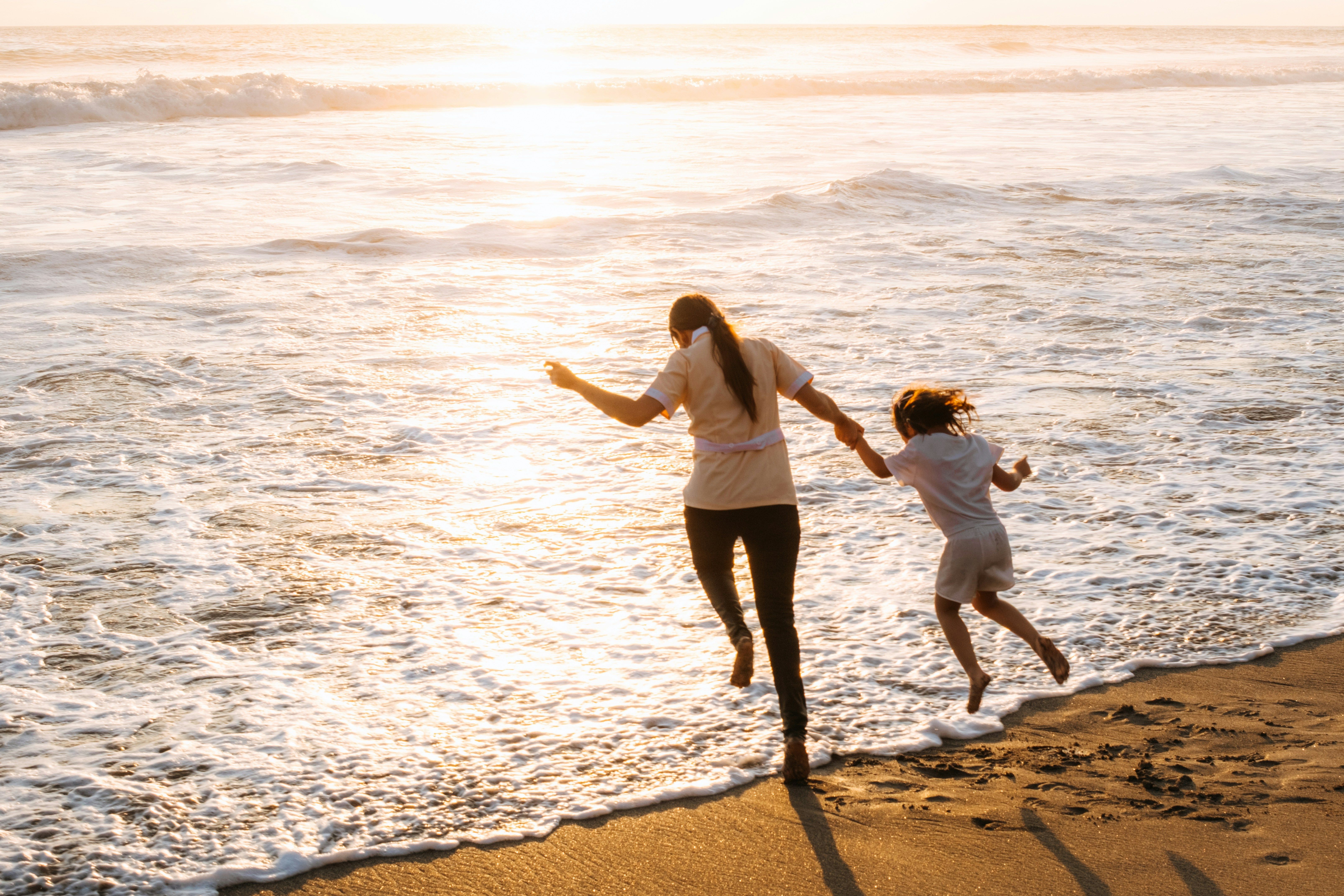 mother and daughter holding hands running into the surf