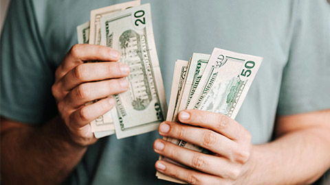 man in green shirt with 2 white hands counting a stack of paper money