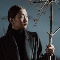 asian person wearing a black coat holding a branch
