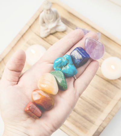 white hand holding 7 colored chakra stones