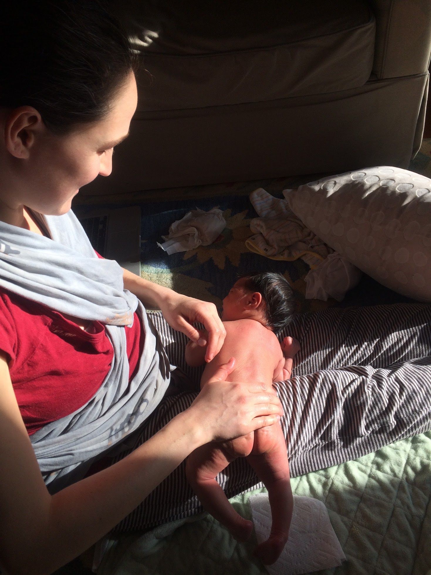Mom with bare newborn baby laid across her lap