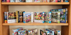 Puzzle Exchange A shelf of jigsaw puzzles of varying sizes sit on a wood shelf unit