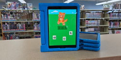iPads An iPad in a blue protective case stands next to three similar iPads on a counter. The iPad displays a game where a cat is shown with scrambled letters to spell cat.