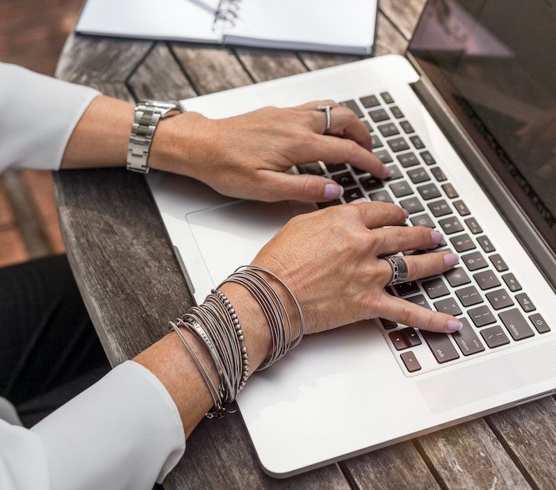 Courtesy of linkedin-sales-navigator-unsplash Woman sitting at outdoor wooden table with computer and silver jewlery