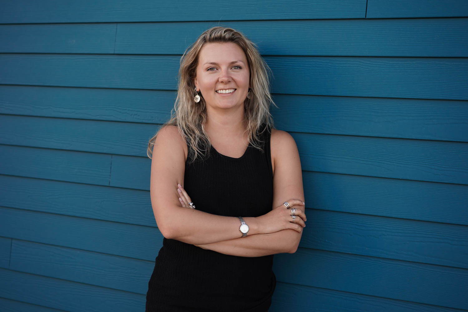 Young woman smiling, leaning against blue wall with arms crossed