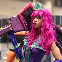 Black woman wearing a pink wig and shiny purple top, holding an over-sized pink axe
