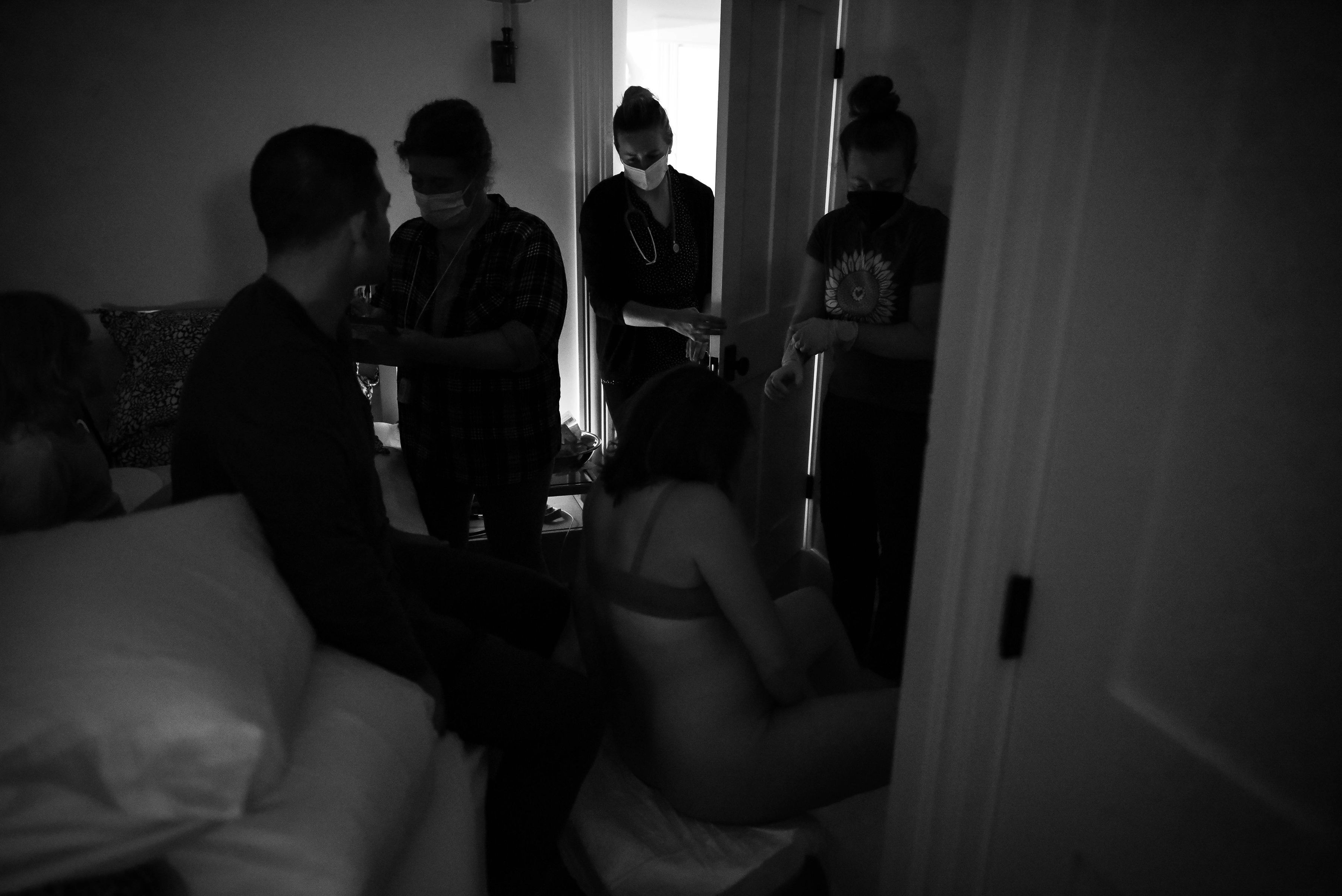 Black and white image of room filled with midwives supporting woman sitting, in labor