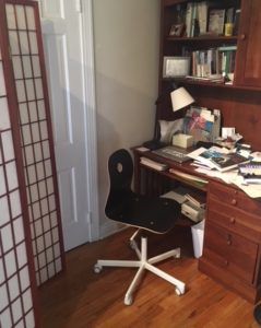 a messy desk with a rolling chair next to a shoji screen