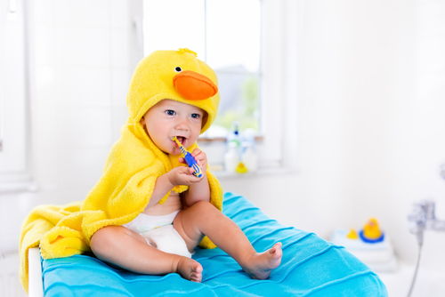 Baby in a yellow duck towel brushing teeth