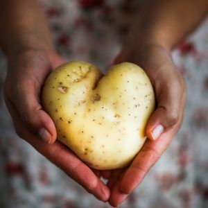 photo of dark skinned hands holding a heart-shaped potato