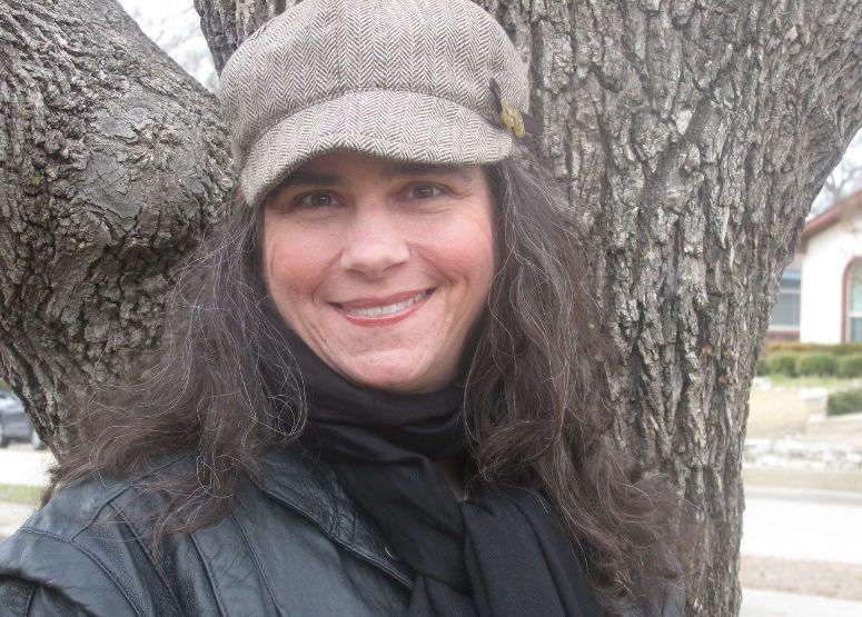 Renee in a winter hat, black scarf, and black jacket in front of a tree